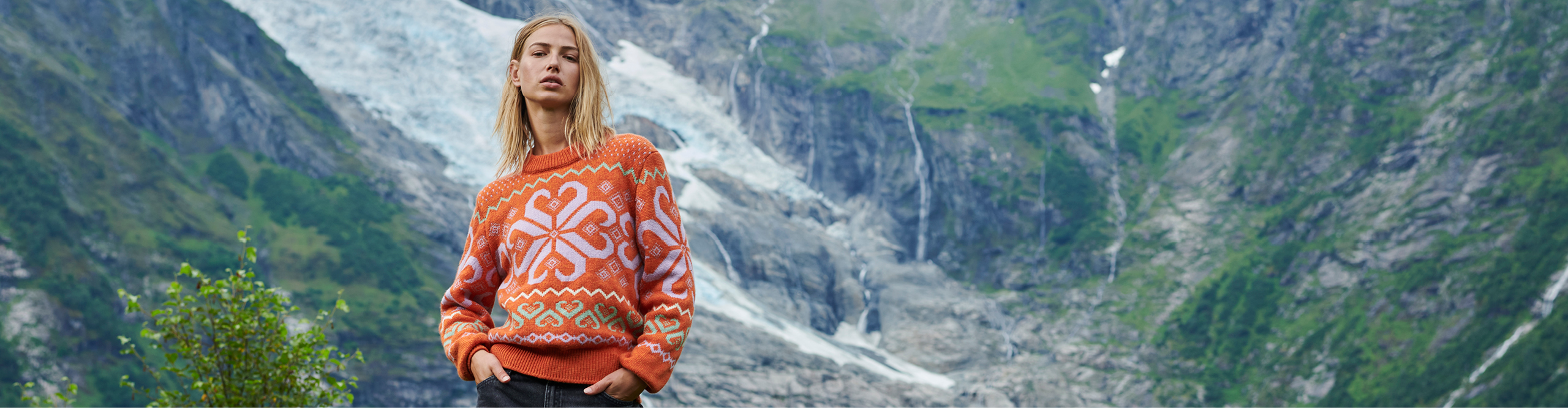 Woman standing in front og glacier wearing Falkeberg sweater in vibrant orange with decorative pattern